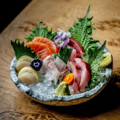 A plate of assorted sashimi, including salmon, tuna, and white fish, garnished with edible flowers, lemon wedges, and wasabi.