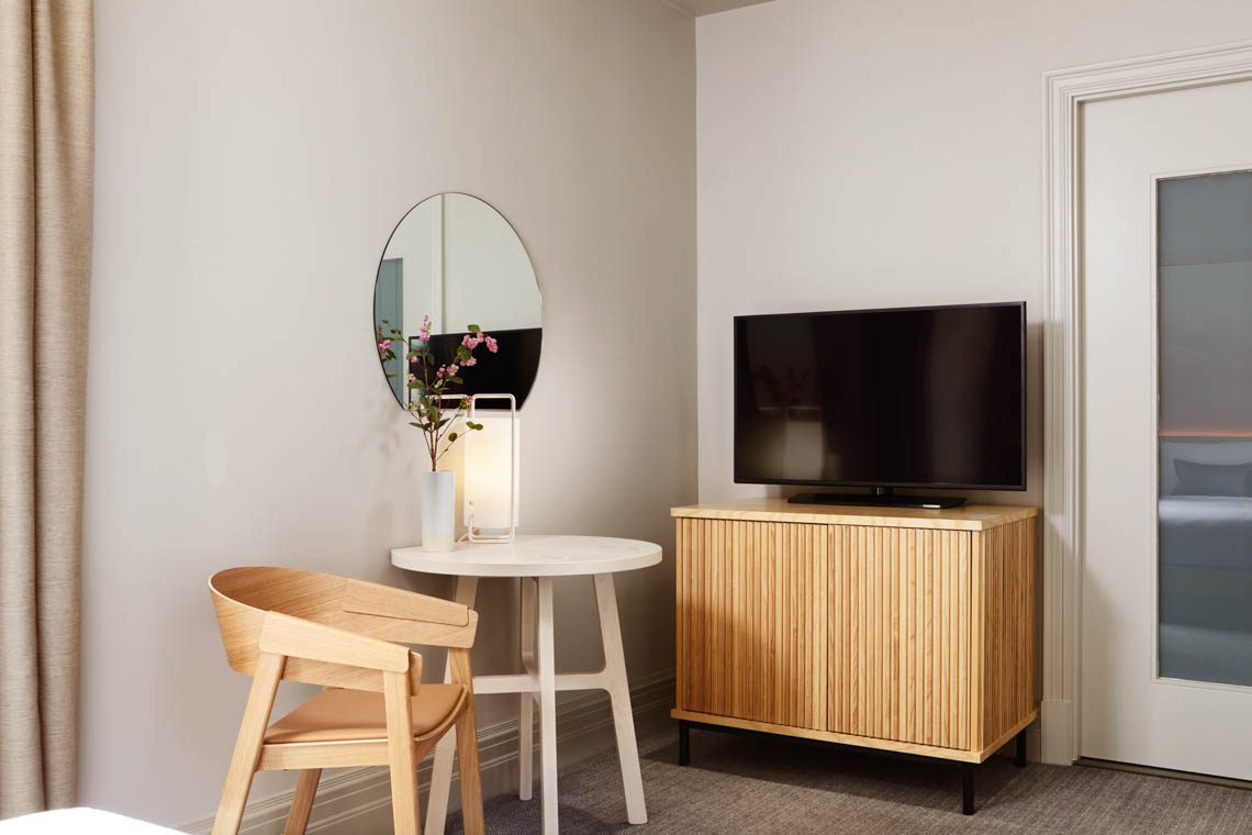 superior-room with a round table, chair, lamp, vase of flowers, mirror, TV, and a cabinet.