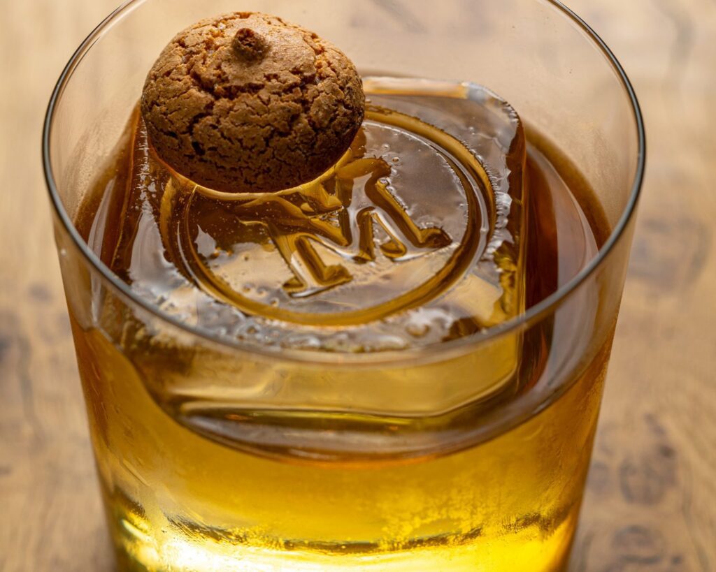Whisky cocktail at The Malt Lounge whisky bar in London featuring a small biscuit and branded ice cube in a small tumbler